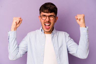 Mor arka planda izole edilmiş genç beyaz bir adam güçlü bir hareket gösteriyor. Kollarıyla, kadınsı gücün sembolü.