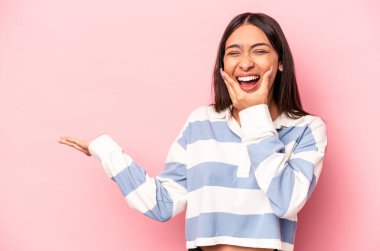 Pembe arka planda izole edilmiş genç İspanyol kadın avuç içinde fotokopi alanı tutuyor, el üstünde tutuyor. Şaşırmış ve mutlu..