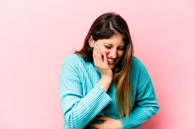 Pembe arka planda izole edilmiş genç beyaz kadın mutlu bir şekilde gülüyor ve ellerini karnının üstünde tutarak eğleniyor..