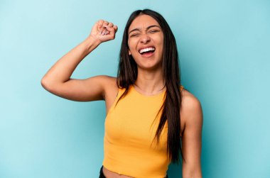 Mavi arka planda izole edilmiş genç İspanyol kadın zaferi, tutkuyu ve coşkuyu, mutlu ifadeyi kutluyor..