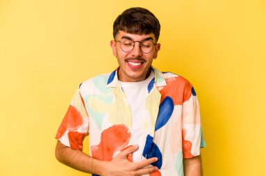 Sarı arka planda izole edilmiş genç beyaz adam karnına dokunur, nazikçe gülümser, yemek yer ve tatmin olur..