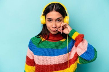 Genç İspanyol kadın mavi arka planda izole edilmiş müzik dinliyor parmakları dudaklarında bir sır saklıyor.