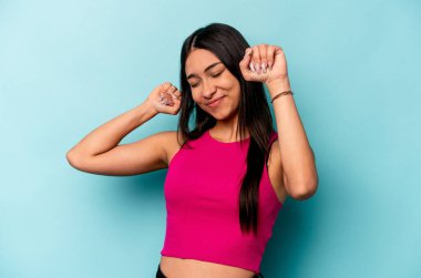 Mavi arka planda izole edilmiş genç İspanyol kadın özel bir günü kutluyor, atlıyor ve enerjiyle kollarını kaldırıyor..