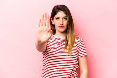 Pembe arka planda izole edilmiş genç beyaz kadın elini uzatmış, dur işareti göstererek seni engelliyor..