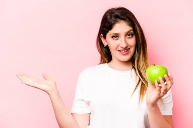 Pembe arka planda bir elma tutan genç beyaz kadın bir avuç içinin fotokopisini çekiyor ve başka bir eli belinde tutuyor..