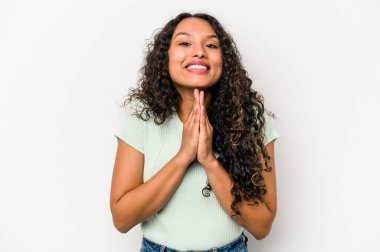 Beyaz arka planda izole edilmiş genç İspanyol bir kadın el ele tutuşup ağzının kenarında dua ediyor, kendinden emin..