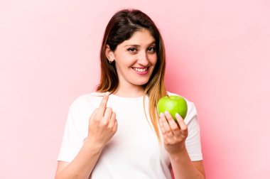 Elma tutan beyaz bir kadın pembe arka planda izole edilmiş bir şekilde seni işaret ediyor sanki davet ediyormuş gibi..