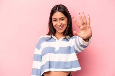 Pembe arka planda izole edilmiş genç İspanyol kadın gülümseyerek beş numarayı parmaklarıyla gösteriyor..