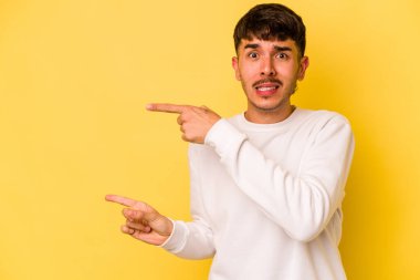 Sarı arka planda izole edilmiş genç beyaz adam işaret parmağıyla fotokopi alanını işaret ederek şok oldu..