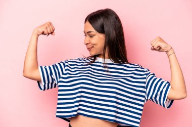 Pembe arka planda izole edilmiş genç İspanyol kadın güçlü bir jest yapıyor, kadınsı gücün sembolü.