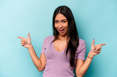 Mavi arka planda izole edilmiş genç İspanyol kadın farklı kopya alanlarını gösteriyor, birini seçiyor, parmaklarıyla gösteriyor..