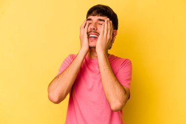 Sarı arka planda izole edilmiş genç beyaz adam ellerini başının üstünde tutarak neşe içinde gülüyor. Mutluluk kavramı.