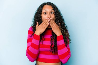 Mavi arka planda izole edilmiş genç İspanyol kadın şok olmuş, ağzı ellerle kaplanmış, yeni bir şey keşfetmeye hevesli..