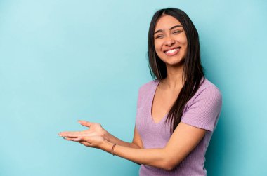 Mavi arka planda izole edilmiş genç İspanyol kadın avucunun içinde bir kopya alanı tutuyor..