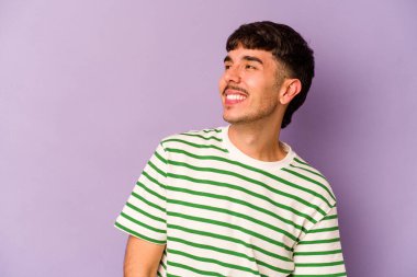 Mor arka planda izole edilmiş genç beyaz adam gevşemiş ve mutlu bir şekilde gülüyor, boynunda dişlerini gösteriyor..