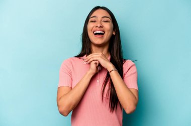 Genç İspanyol kadın mavi arka planda izole edilmiş şans için dua ediyor, şaşırmış ve ağzını açıp önüne bakıyor..