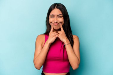 Mavi arka planda izole edilmiş genç İspanyol kadın iki seçenek arasında şüphe duyuyor.