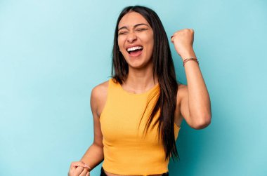 Genç İspanyol kadın mavi arka planda izole edilmiş kaygısız ve heyecanlı tezahüratlar yapıyor. Zafer konsepti.