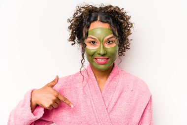 Yüz maskesi takan genç İspanyol bir kadın beyaz arka planda izole edilmiş. Elle bir gömlek fotokopi alanını işaret ediyor. Gururlu ve kendinden emin.