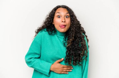 Beyaz arka planda izole edilmiş genç İspanyol kadın karnına dokunuyor, nazikçe gülümsüyor, yemek yiyor ve tatmin oluyor..