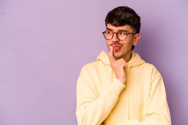 Mor arka planda izole edilmiş genç beyaz adam şüpheli ve şüpheci bir ifadeyle yana bakıyor..