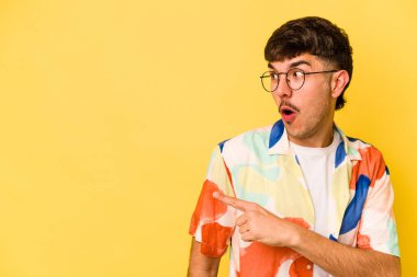 Kafkasyalı genç adam sarı arka planda izole edilmiş, başparmak uzakta, gülüyor ve kaygısız..