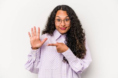 Beyaz arka planda izole edilmiş genç İspanyol kadın gülümseyerek beş numarayı parmaklarıyla gösteriyor..