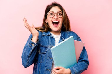 Pembe arka planda izole genç beyaz kadın hoş bir sürpriz alıyor, heyecanlı ve el kaldırıyor..