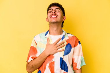 Sarı arka planda izole edilmiş genç beyaz adam yüksek sesle gülüyor ve elini göğsüne koyuyor..