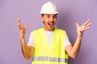 Genç İspanyol işçi, mor arka planda izole edilmiş. Hoş bir sürpriz bekliyor. Heyecanlı ve el kaldırıyor..