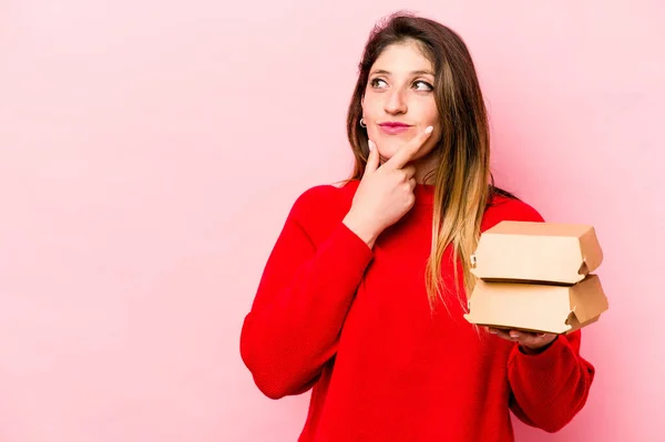 Jonge Kaukasische Vrouw Houden Hamburgers Geïsoleerd Roze Achtergrond Kijken Zijwaarts — Stockfoto