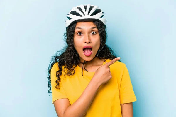若いですヒスパニック系の女性は サイドを指して青い背景に隔離ヘルメット自転車を着て — ストック写真