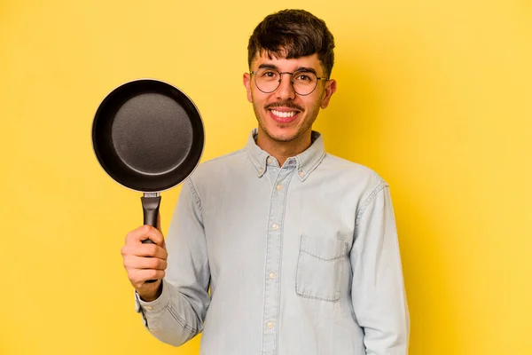 黄色の背景に孤立したフライパンを保持若いヒスパニック系の炊飯器幸せ 笑顔と陽気 — ストック写真