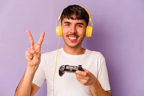 若いですヒスパニック男再生とともにビデオゲームコントローラ孤立紫色の背景番号2とともに指 — ストック写真