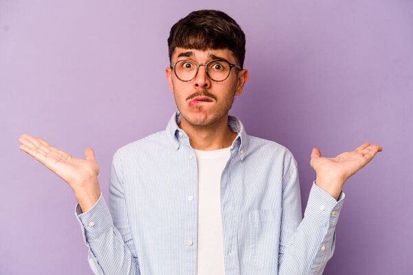 Young caucasian man isolated on purple background confused and doubtful shrugging shoulders to hold a copy space.