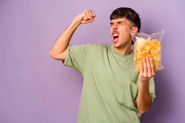 Jonge Spaanse Man Met Chips Geïsoleerd Paarse Achtergrond Hef Vuist — Stockfoto