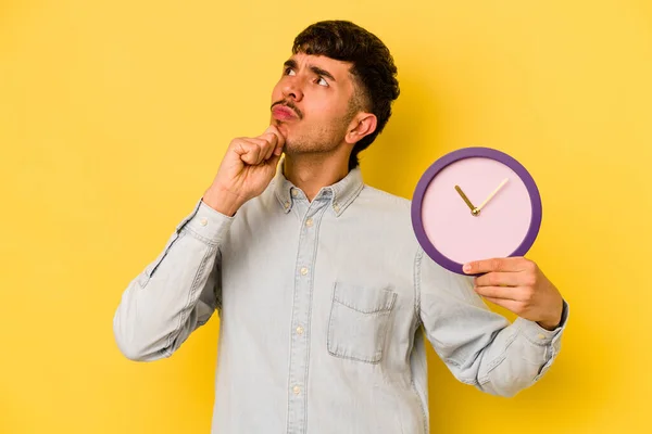 Young Hispanic Man Holding Clock Isolated Yellow Background Looking Sideways — Stock Photo, Image