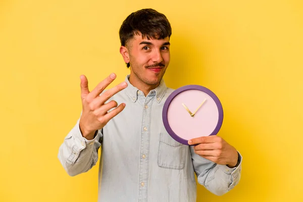 Jovem Hispânico Segurando Relógio Isolado Fundo Amarelo Apontando Com Dedo — Fotografia de Stock