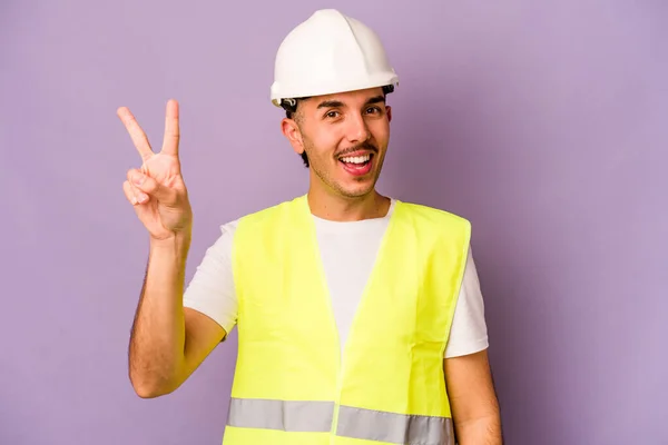 Young hispanic worker man isolated on purple background joyful and carefree showing a peace symbol with fingers.