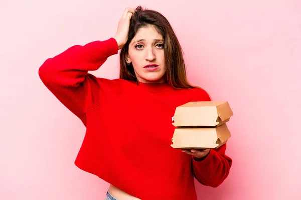 Junge Kaukasische Frau Hält Burger Isoliert Auf Rosa Hintergrund Schockiert — Stockfoto