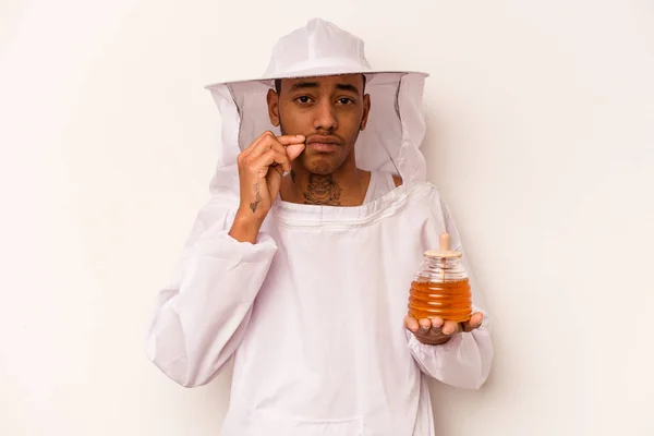 Young African American beekeeper isolated on white background with fingers on lips keeping a secret.