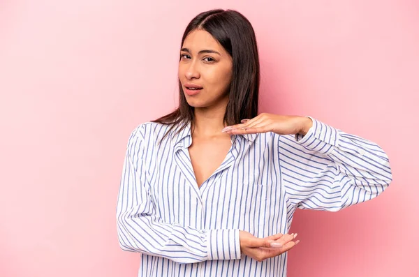 Pembe arka planda izole edilmiş genç İspanyol kadın iki eliyle bir şey tutuyor, ürün sunumu..