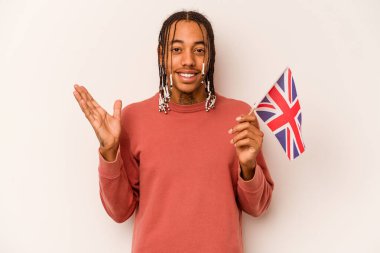 Beyaz arka planda İngiliz bayrağı tutan genç bir Afrikalı Amerikalı hoş bir sürpriz alıyor, heyecanlı ve el kaldırıyor..