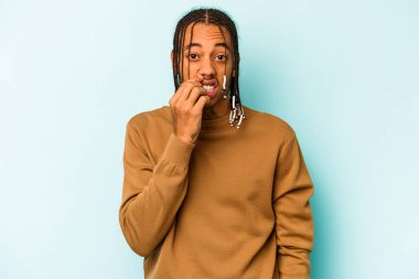 Genç Afrikalı Amerikalı bir adam mavi arka planda izole edilmiş tırnak yiyor, gergin ve çok endişeli..