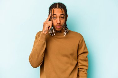 Genç Afrikalı Amerikalı bir adam mavi arka planda izole edilmiş. Parmağıyla tapınağı işaret ediyor. Düşünüyor, bir göreve odaklanıyor..