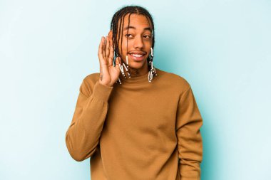 Genç Afrikalı Amerikalı bir adam mavi arka planda izole edilmiş bir şekilde bir dedikoduyu dinlemeye çalışıyor..
