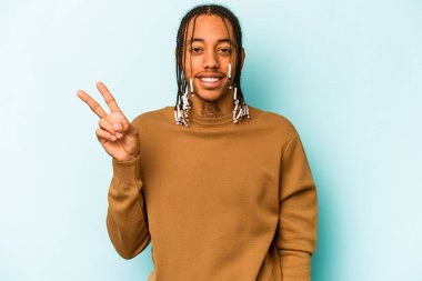 Genç Afrikalı Amerikalı adam mavi arka planda izole edilmiş neşeli ve kaygısız parmakları olan bir barış sembolü gösteriyor..
