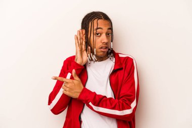 Genç Afrikalı Amerikalı adam beyaz arka planda izole edilmiş bir şekilde bir dedikoduyu dinlemeye çalışıyor..