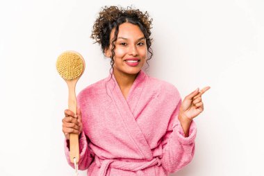 Beyaz arka planda izole edilmiş sırt kaşıyıcısı tutan genç İspanyol kadın gülümsüyor ve boş alanda bir şeyler gösteriyor..