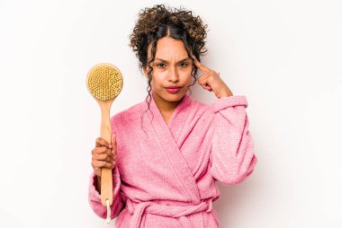 Sırt kaşıyıcısını tutan genç İspanyol kadın beyaz arka planda izole edilmiş, parmağıyla tapınağı işaret ediyor, düşünüyor, bir göreve odaklanıyor..